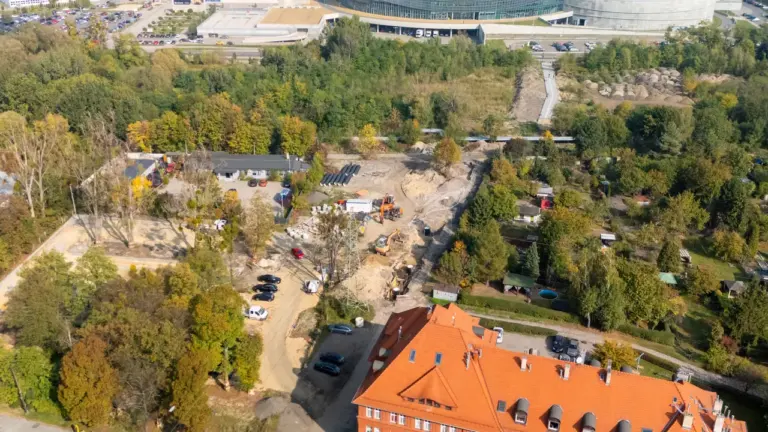 Widok z lotu ptaka na plac budowy przy ceglanym budynku obok nowoczesnej hali sportowej.